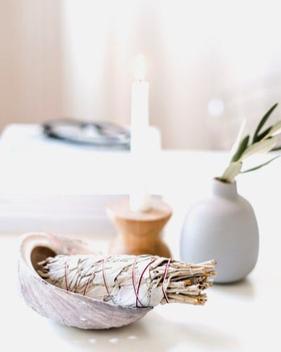 a white sage smudge stick in a bowl next to a candle